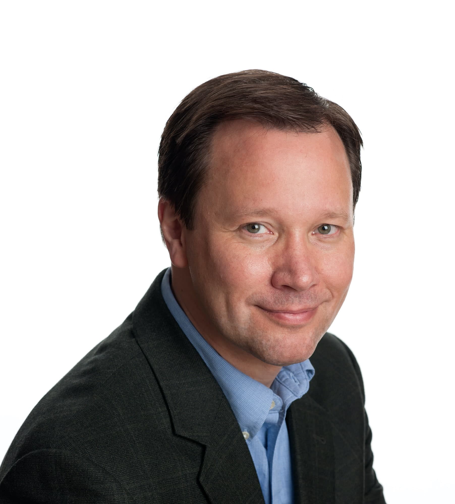 A man with short brown hair wearing a dark blazer and blue shirt, smiling slightly, poses against a white background.