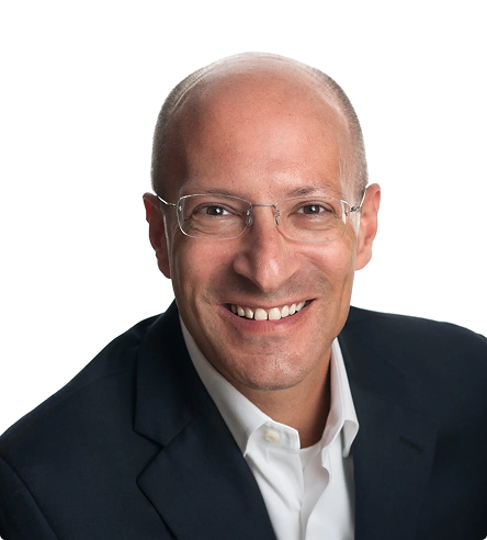 A smiling man in a dark suit jacket and white shirt, wearing glasses, with a bald head, poses against a plain white background.